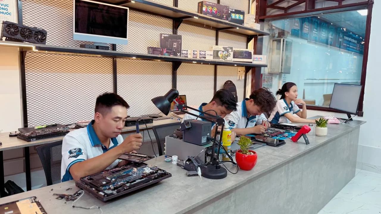 Bàn kỹ thuật tại tiệm RIGPC với laptop đã tháo vỏ, trạm hàn và đèn soi